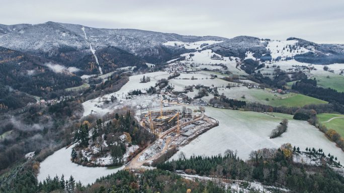 Landschaft mit schneebedeckten Hügeln, Wäldern und einem kleinen Dorf im Tal.