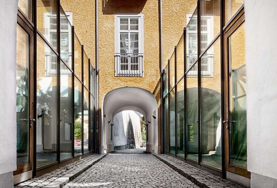 Durchgang mit spiegelnden Fenstern und gelber Wand in einer schmalen Gasse.